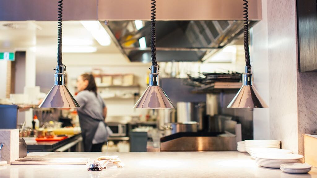 Side view of unrecognizable female chef in restaurant kitchen working behind counter with infrared lamps and serving kitchenware